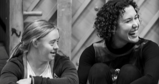 A black and white photo of Hannah Sampson and Amy Butler, they both look to their left, Amy has a big grin.