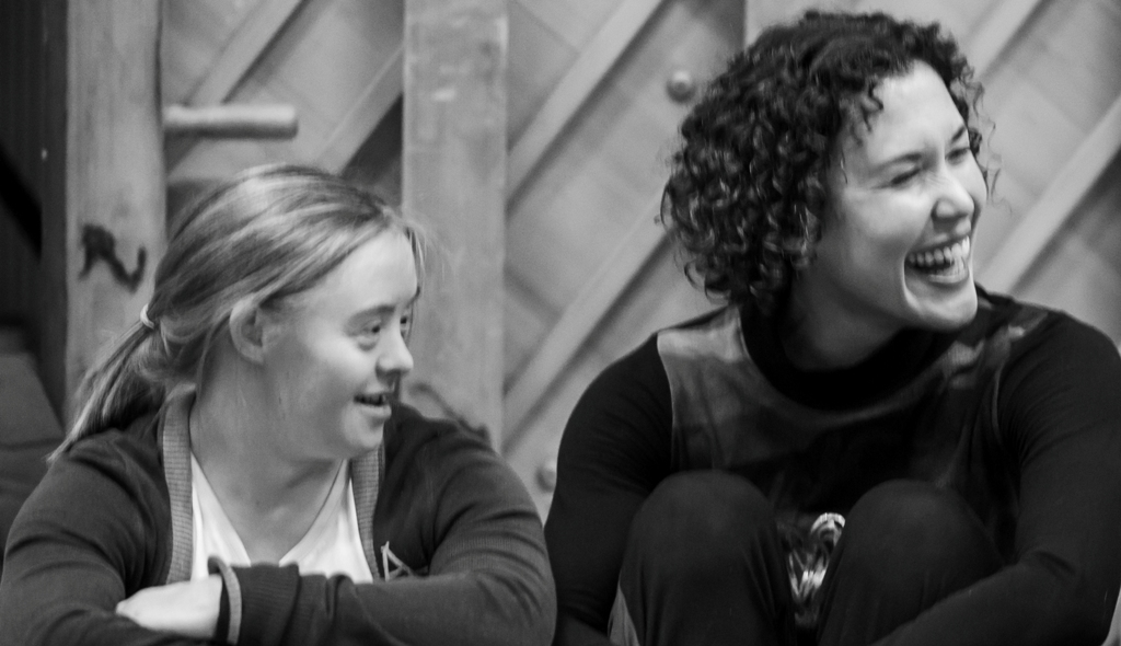 A black and white photo of Hannah Sampson and Amy Butler, they both look to their left. Amy has a big grin on her face.