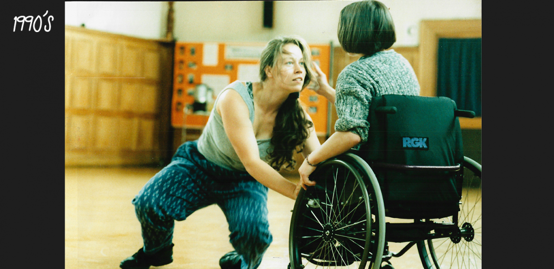 A photo of Vicki Balaam in duet with a dancer in a wheelchair who has their back to the camera.