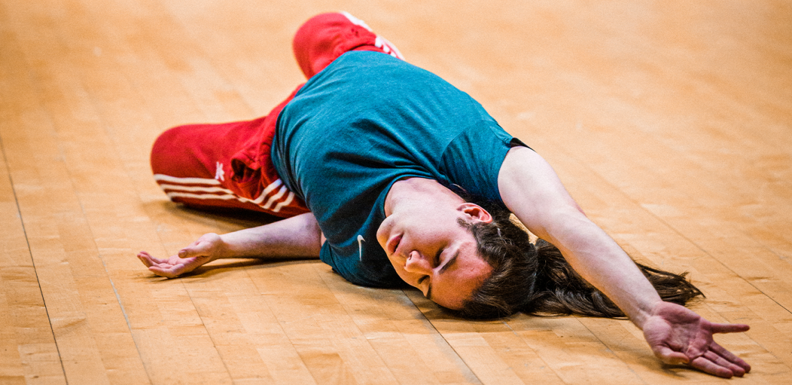 ID: A photo of Fin dancing on the floor, he lays down reaching an arm above his head, eyes closed.