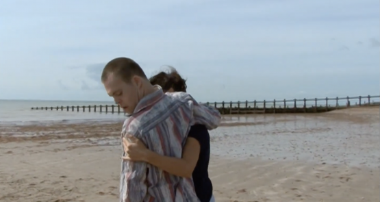 Chris and Lucy embrace on a beach.
