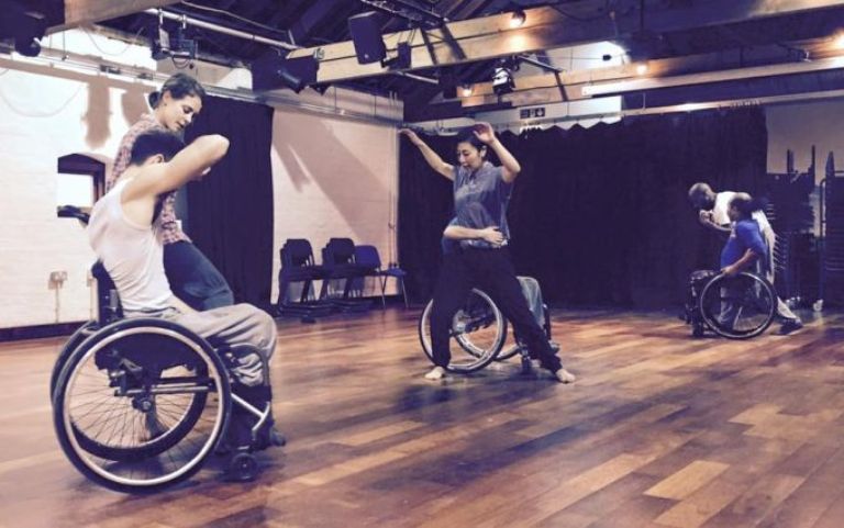 A group of 3 standing and 3 wheelchair dancers in a studio.
