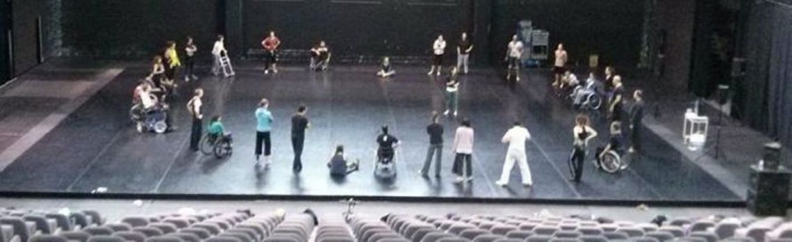 A photo of a group of dancers forming a circle on a stage, taken from high up in the auditorium