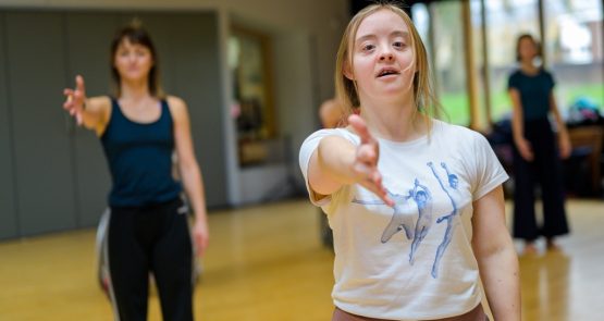 Two dancers in the studio, extending their right hands towards the camera