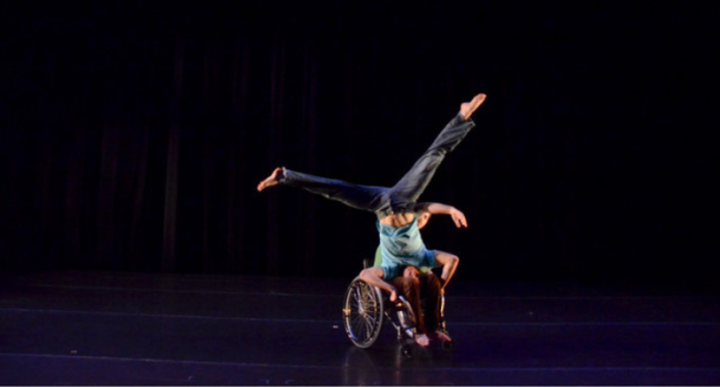 One dancer balanced upside down on the lap of a wheelchair dancer