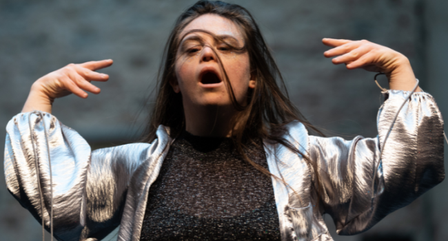 A learning Disabled dancer, hair partially over their face and hands raised