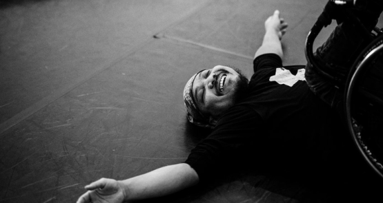 A black and white photo of a wheelchair dancer resting on their back on the floor.