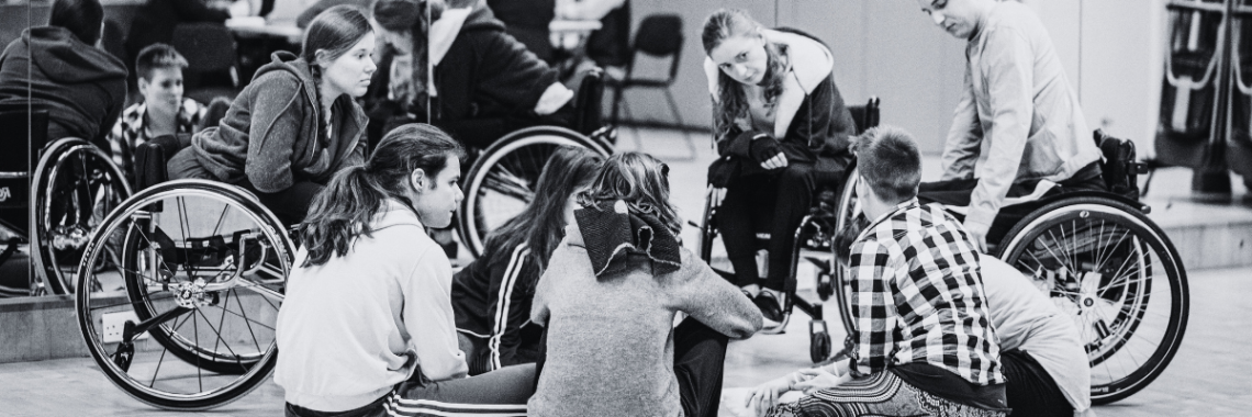 A black and white photo of a group of Disabled and non-disabled dancers in discussion.
